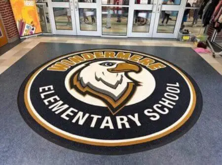 Large custom-sized entrance rug with school logo centered in a wide double-door lobby.