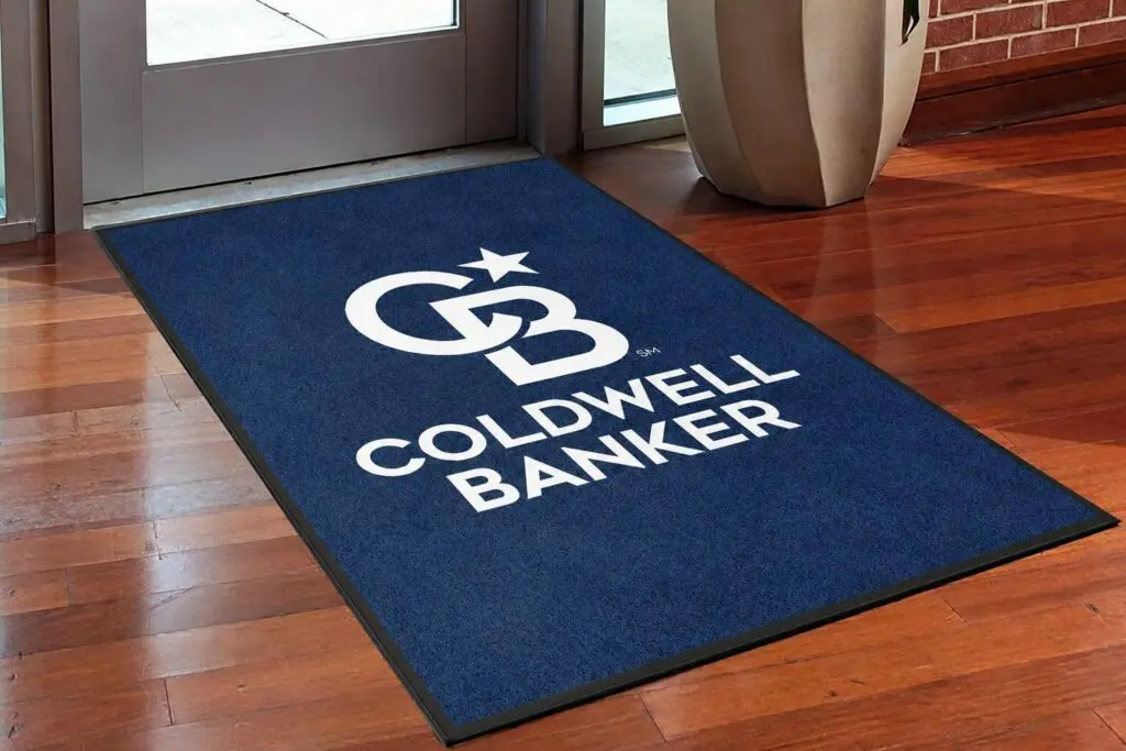 Coldwell Banker custom DigiPrint HD navy blue logo mat with white brand logo installed at real estate office lobby entrance on hardwood floor