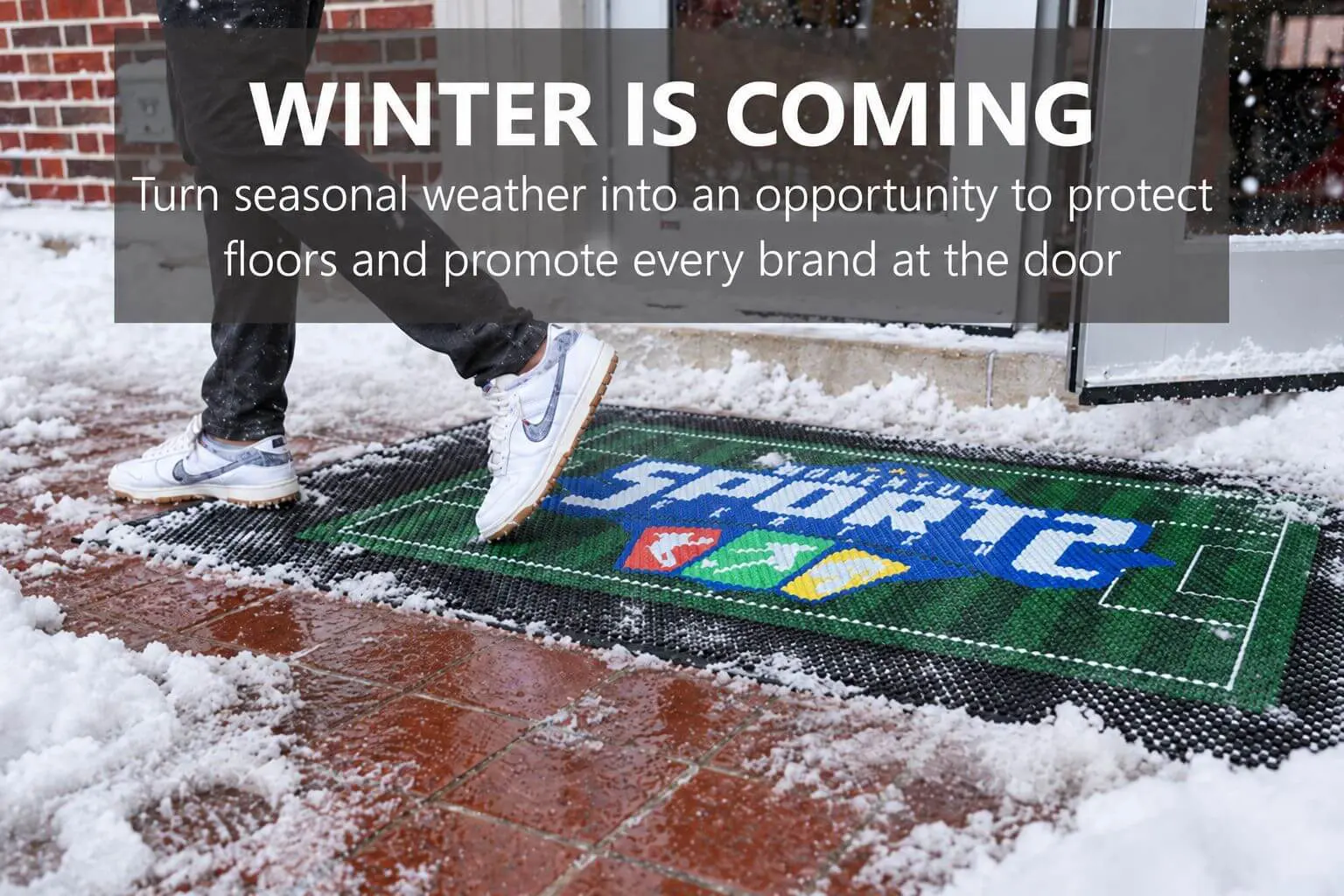 Snowy commercial entrance with branded scraper mat catching snow and salt before it enters the building